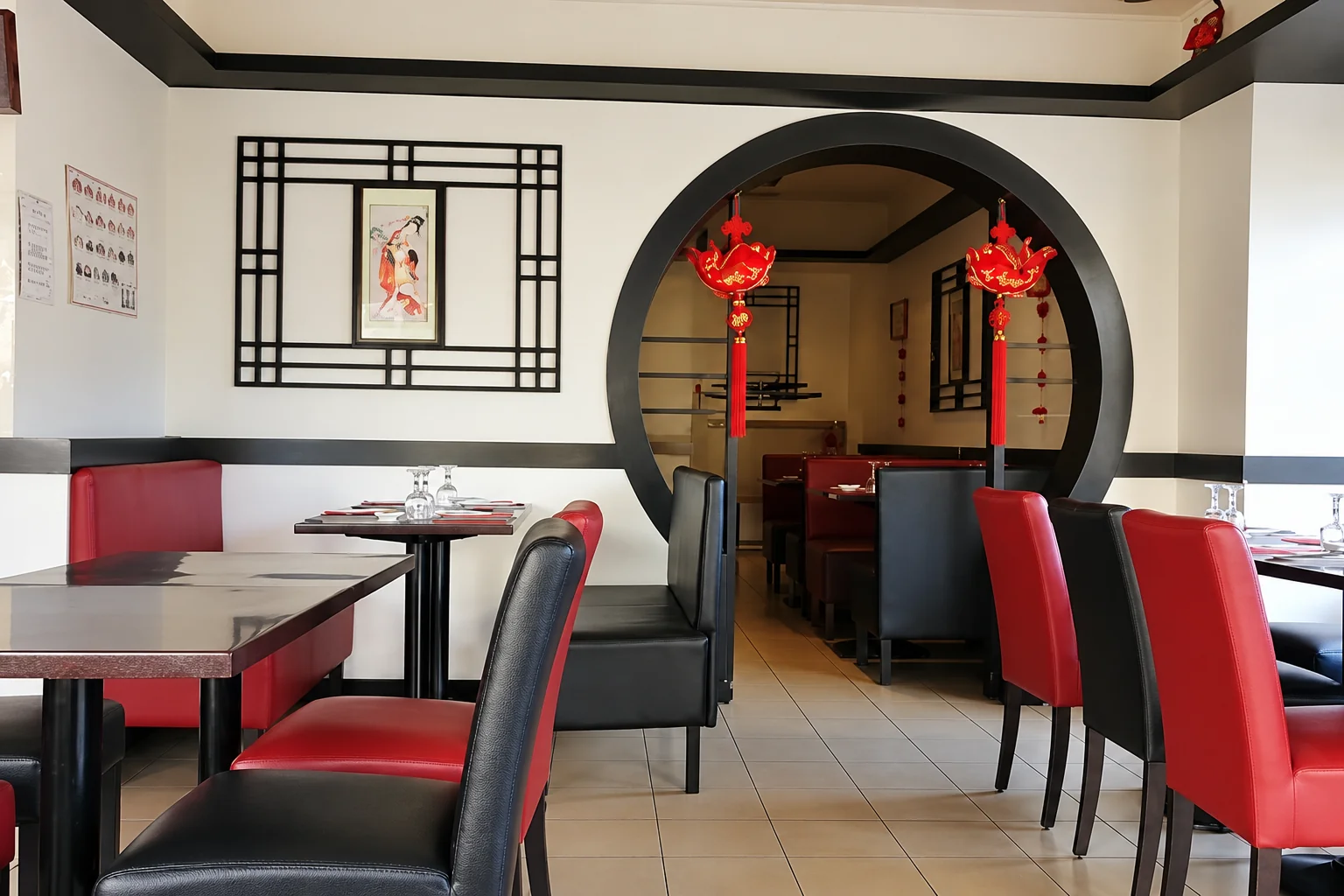 Dining room with a round doorway, red lanterns, black tables and red and black chairs.