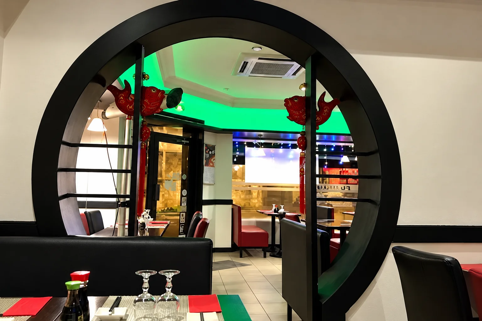 Black round doorway with red decorations, a green-lit room behind, glasses on the table.