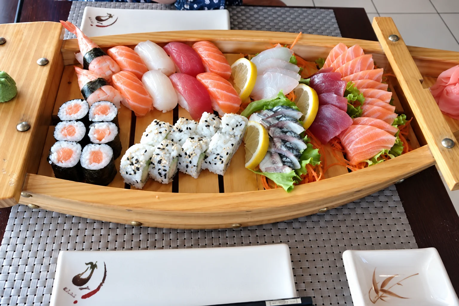 Wooden boat with sushi, maki, california rolls and sashimi, on a table.