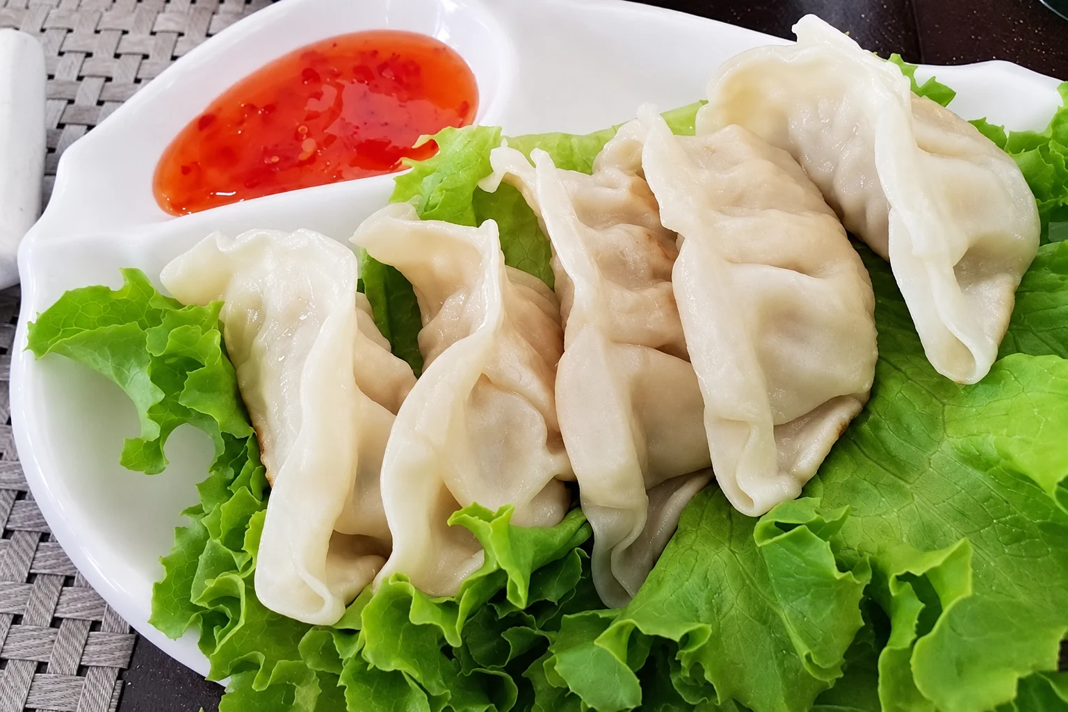 Dumplings on lettuce leaves, red sauce in a small dish, white plate.